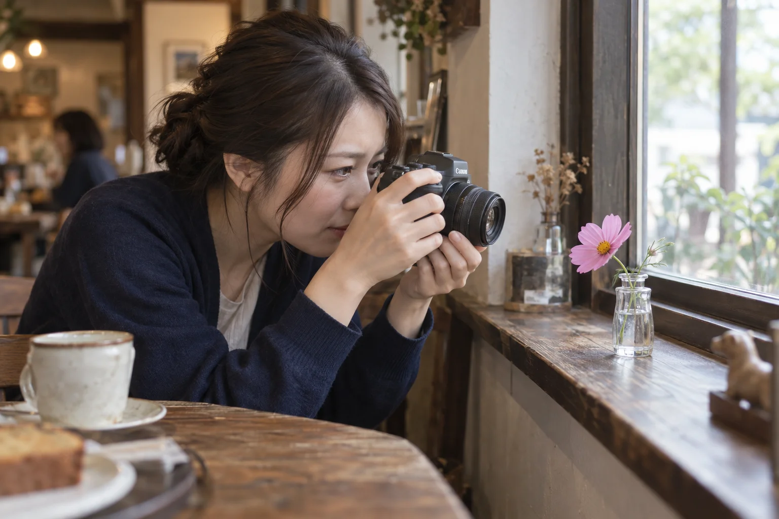 カフェの窓辺で、小さな花瓶のコスモスへ単焦点レンズを向けて撮る人