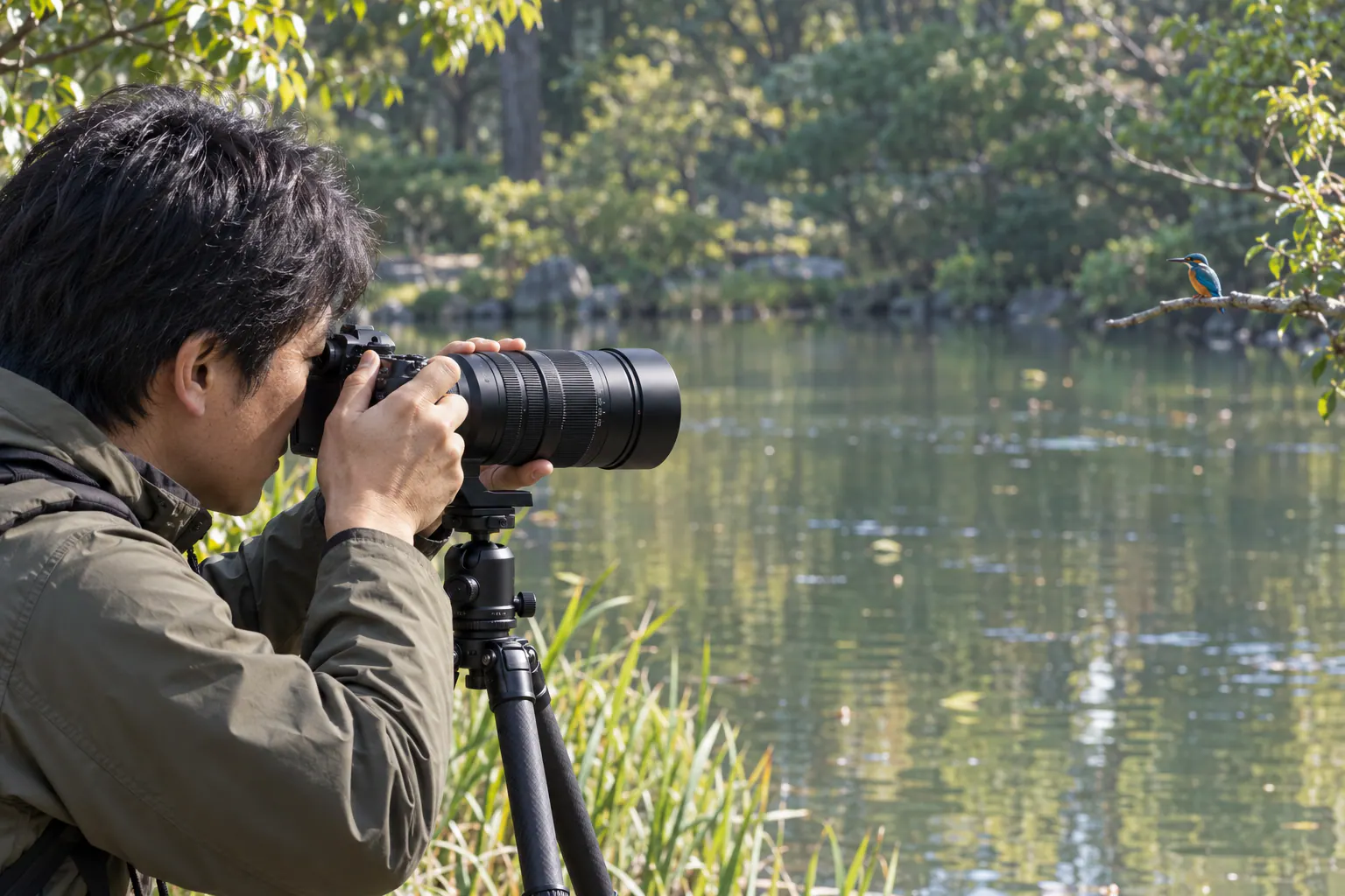LEICA DG 100–400mm II付きカメラを三脚に載せ、水辺のカワセミへ向ける撮影者