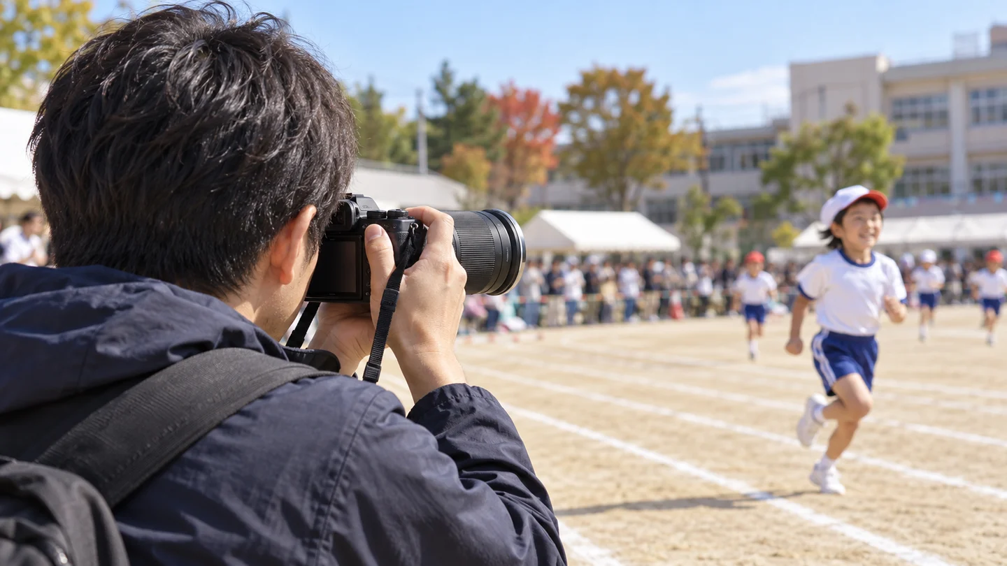 ファインダーをのぞいた親が望遠レンズを走る子どもへ向けて運動会を撮る場面