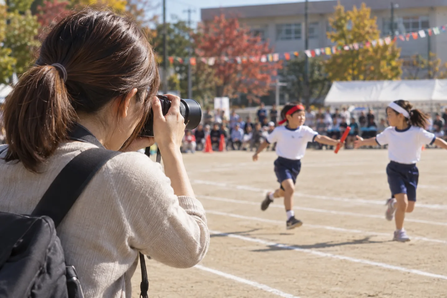 運動会のリレーを軽い望遠ズームで撮る母親