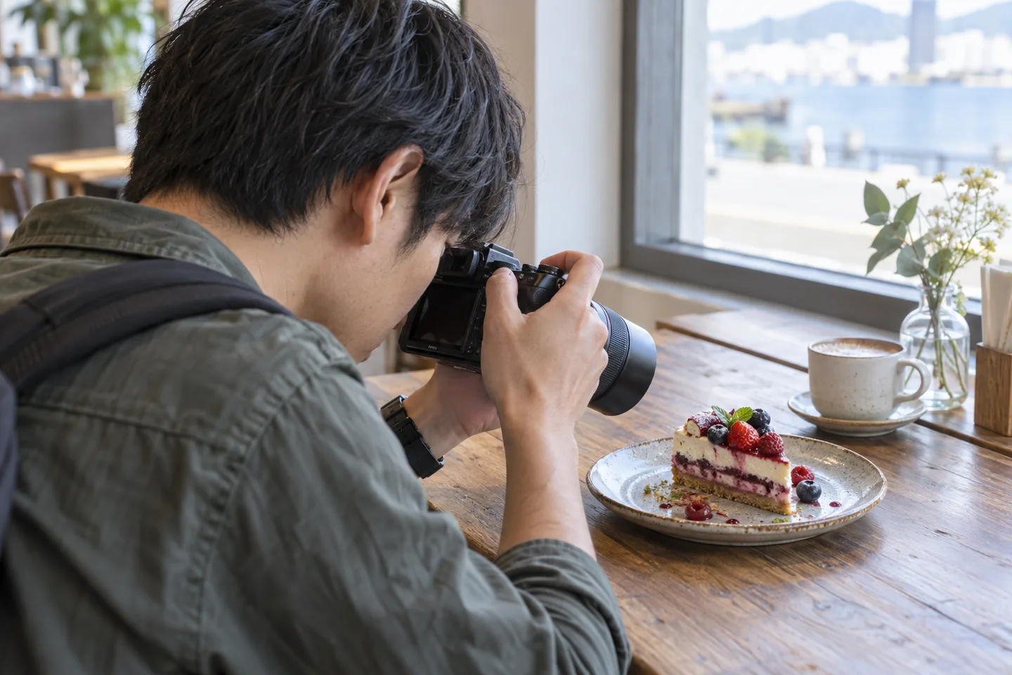 窓辺のテーブルでケーキへカメラを近づけて撮る旅行者
