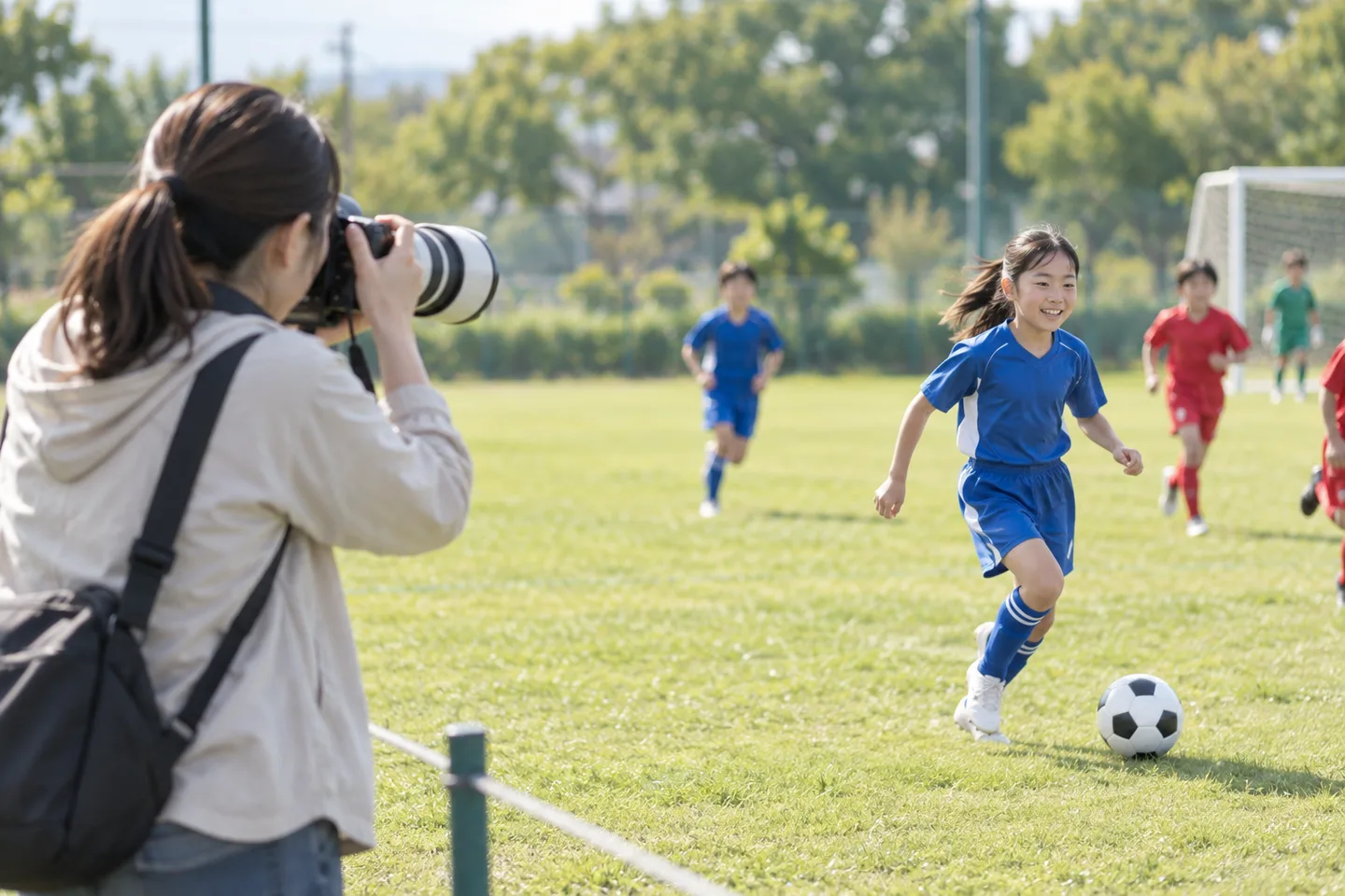 タッチラインの外からサッカーをする子どもへ望遠レンズを向ける母親