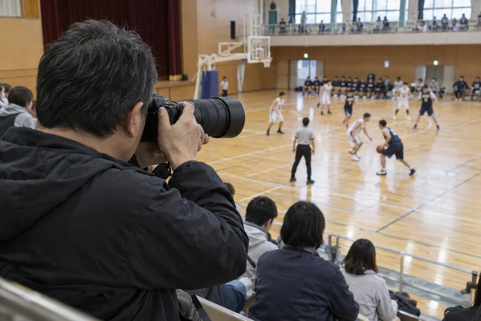 体育館の観客席からバスケットボールを望遠レンズで撮る人